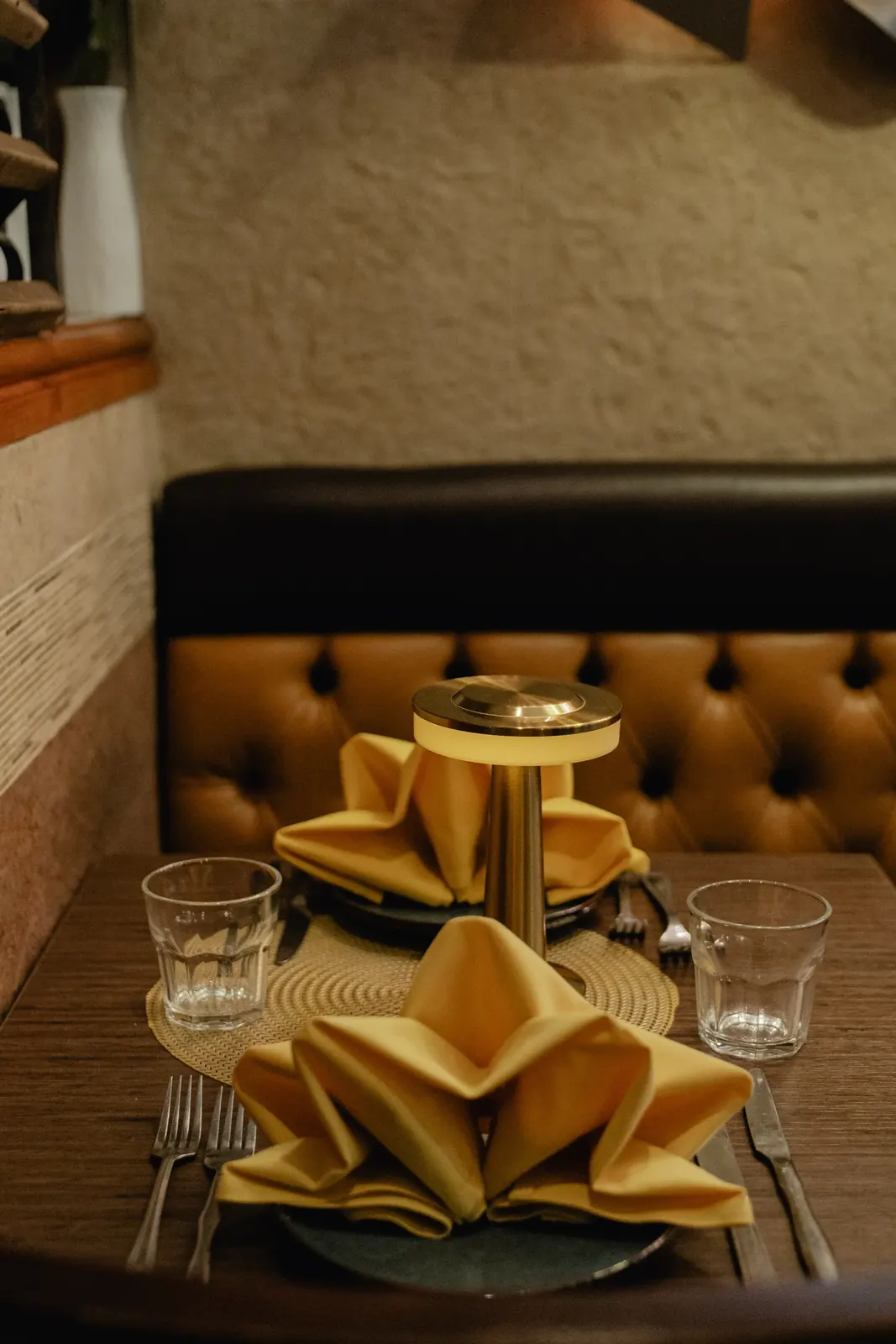 An intimate table setting with folded napkins and a brass table lamp
