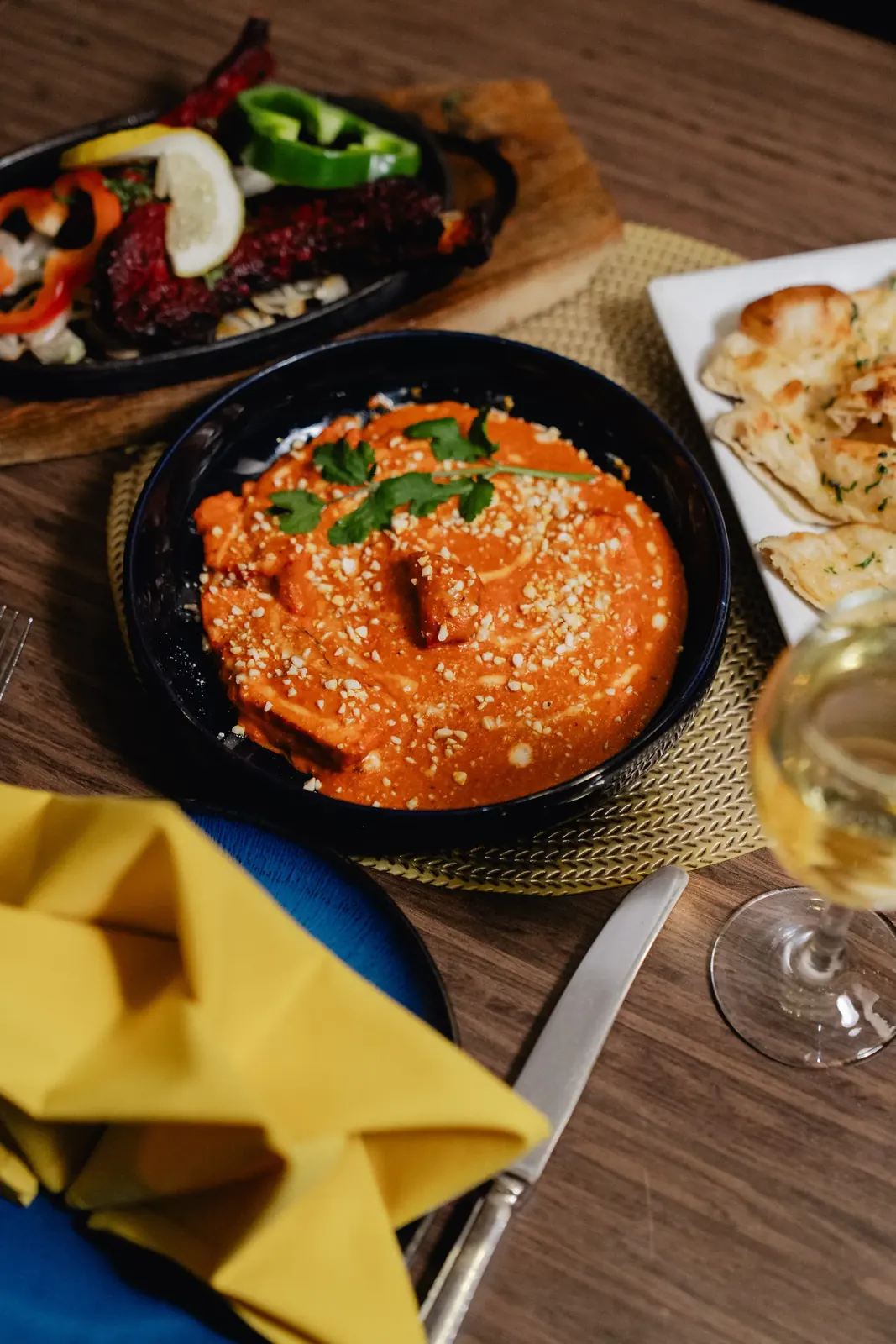 A creamy tomato curry topped with crushed nuts and coriander, served with garlic naan and white wine
