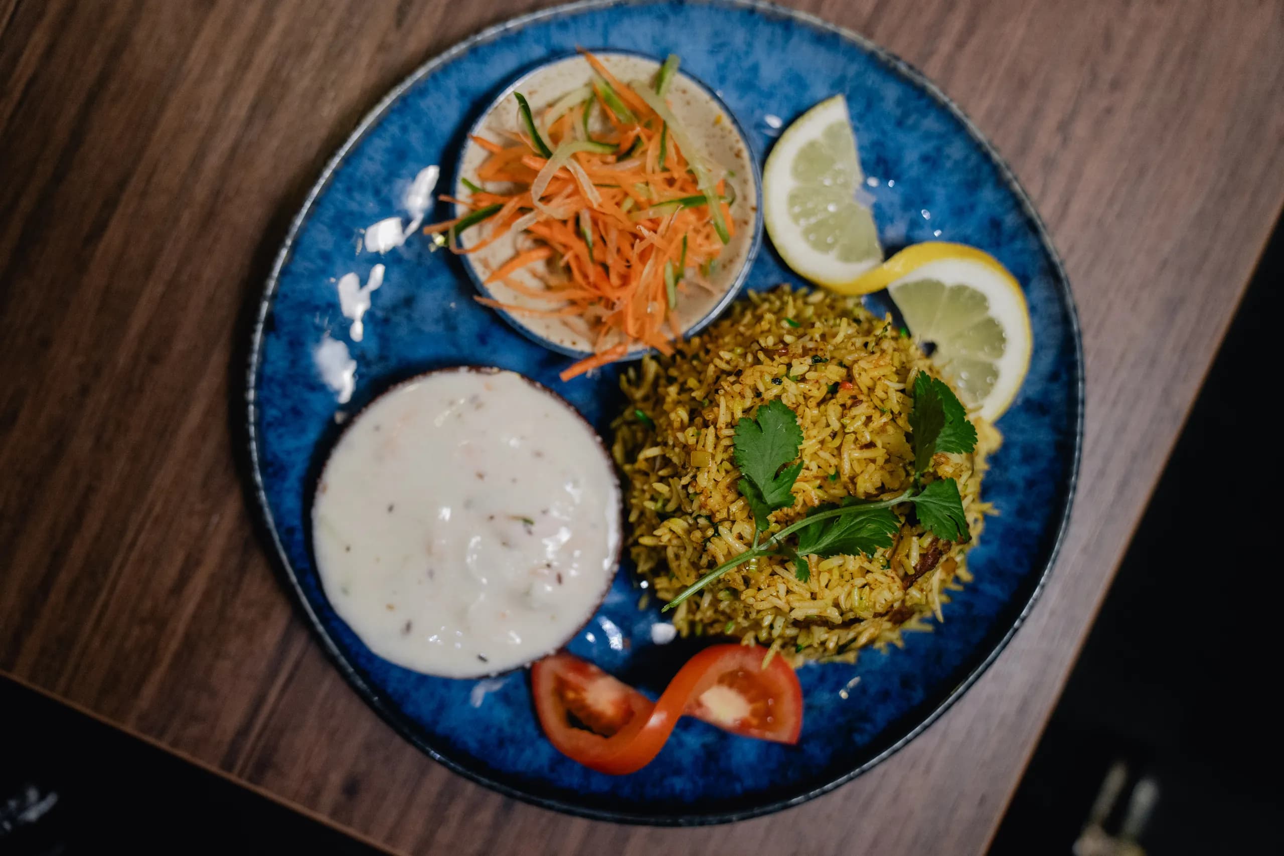 Biryani served with raita and salad on a blue plate