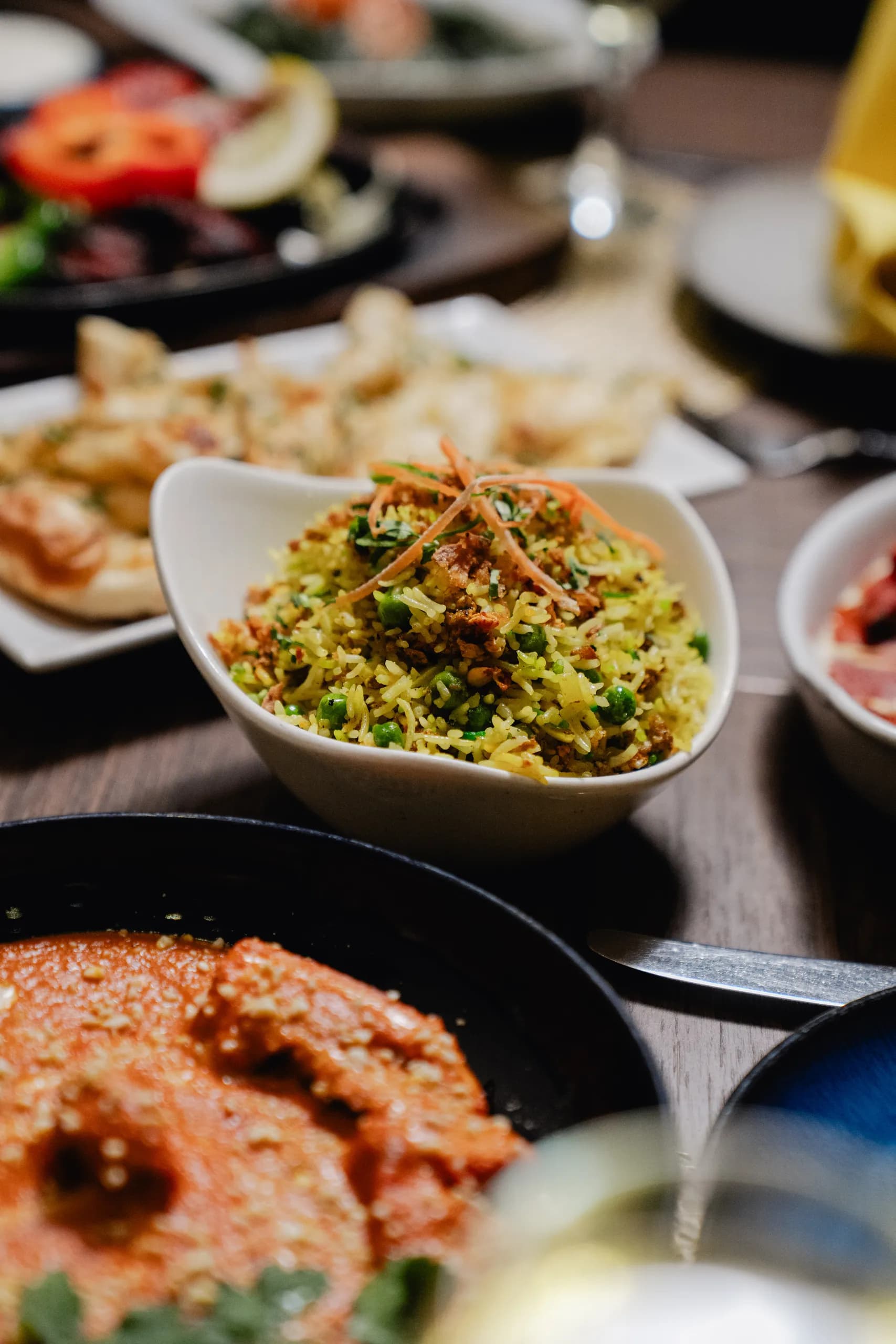 A bowl of pilau rice with peas and crispy onions, with naan and a creamy curry alongside