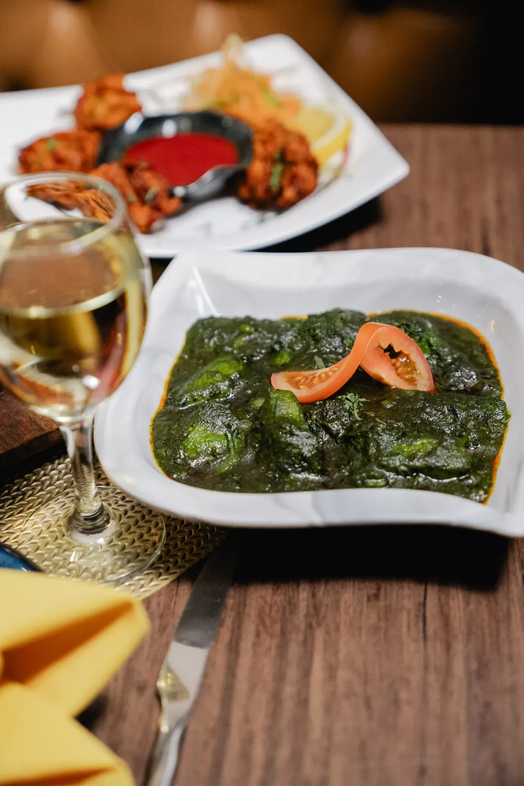 Spinach saag topped with fresh tomato, with a plate of onion bhajis behind