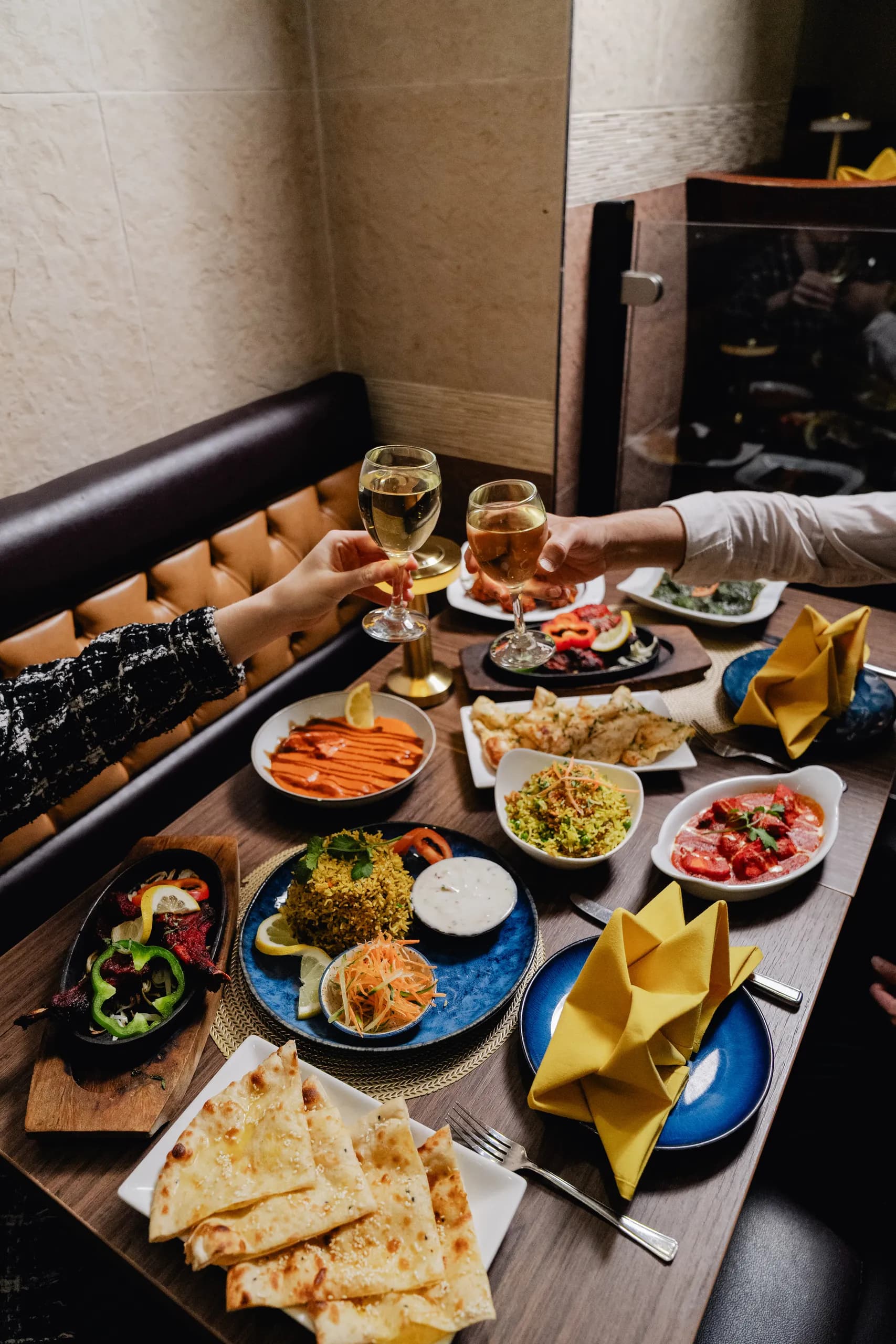 Two diners toasting with white wine over a table of curries, naan, pilau rice and a tandoori sizzler